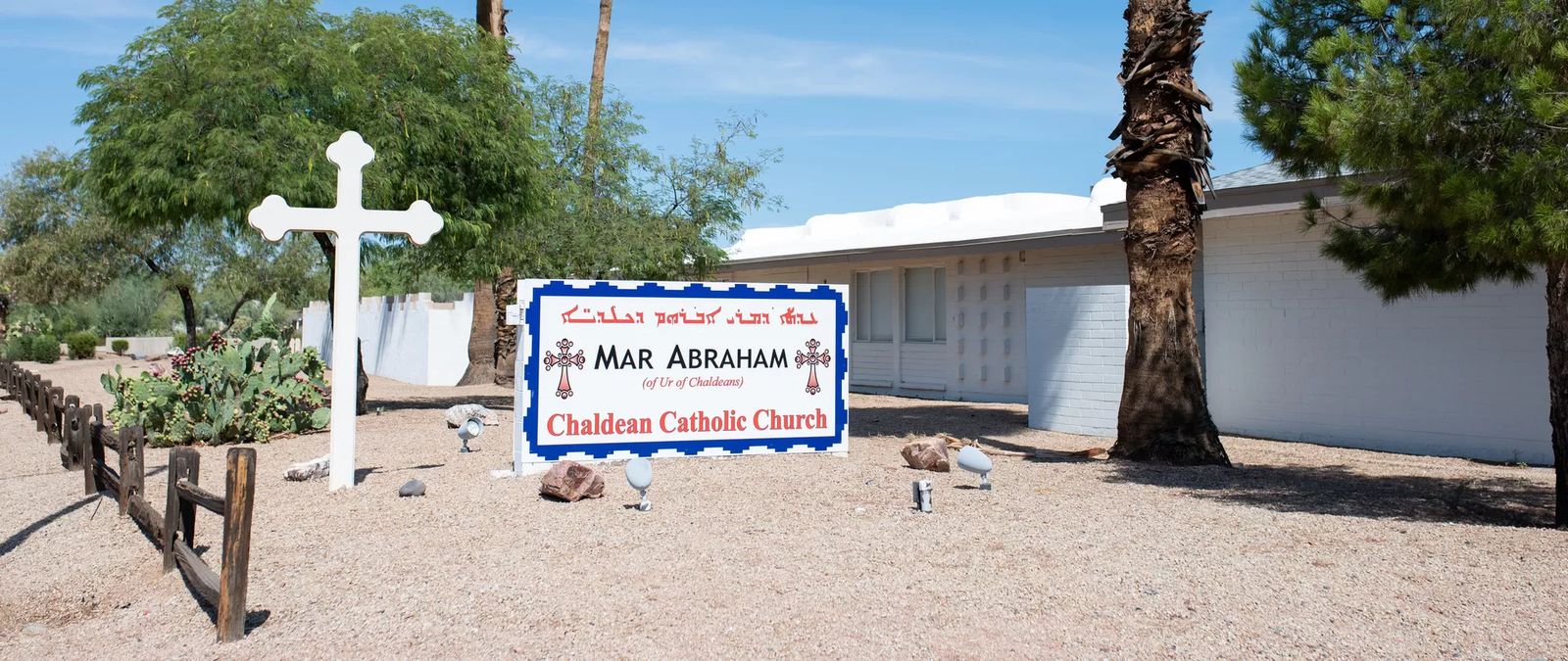 A white cross and the sign in front of Mar Abraham Chaldean Catholic Church
