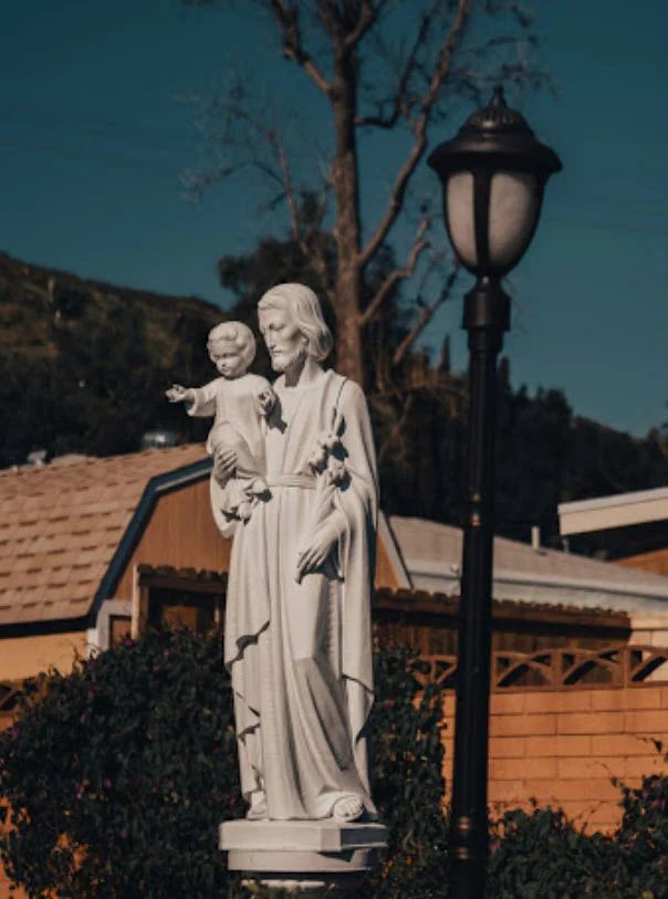 A statue of St. Joseph holding the Christ Child beside a lamp at dusk